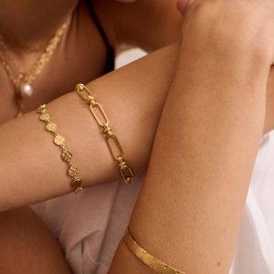 Gold-plated chain bracelet, charm bracelet, and bangle styled on a woman's arm.